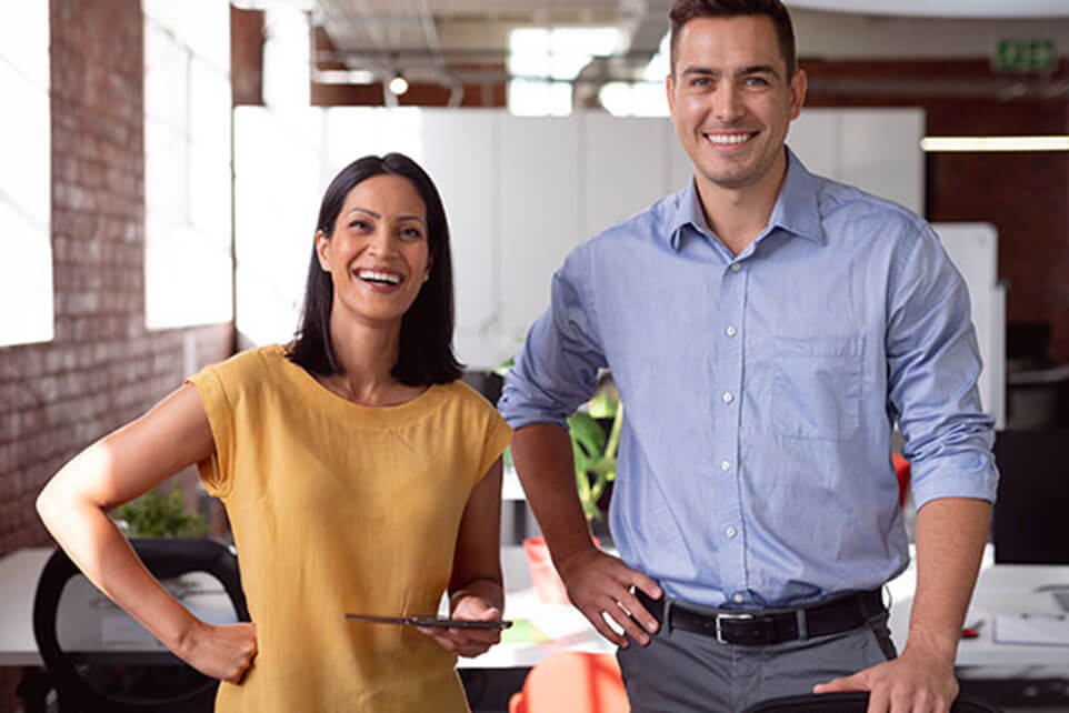 Portrait of happy caucasian male and female colleague standing at desk smiling