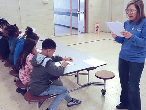 Armor Bank Team member reading to children in a school cafeteria.