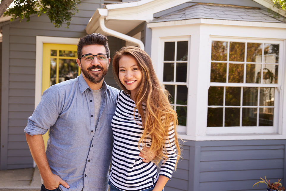 A young couple taking a photo in front of their new home.