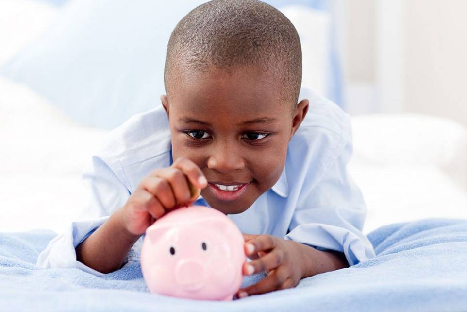 Young child putting coins in a piggy bank.