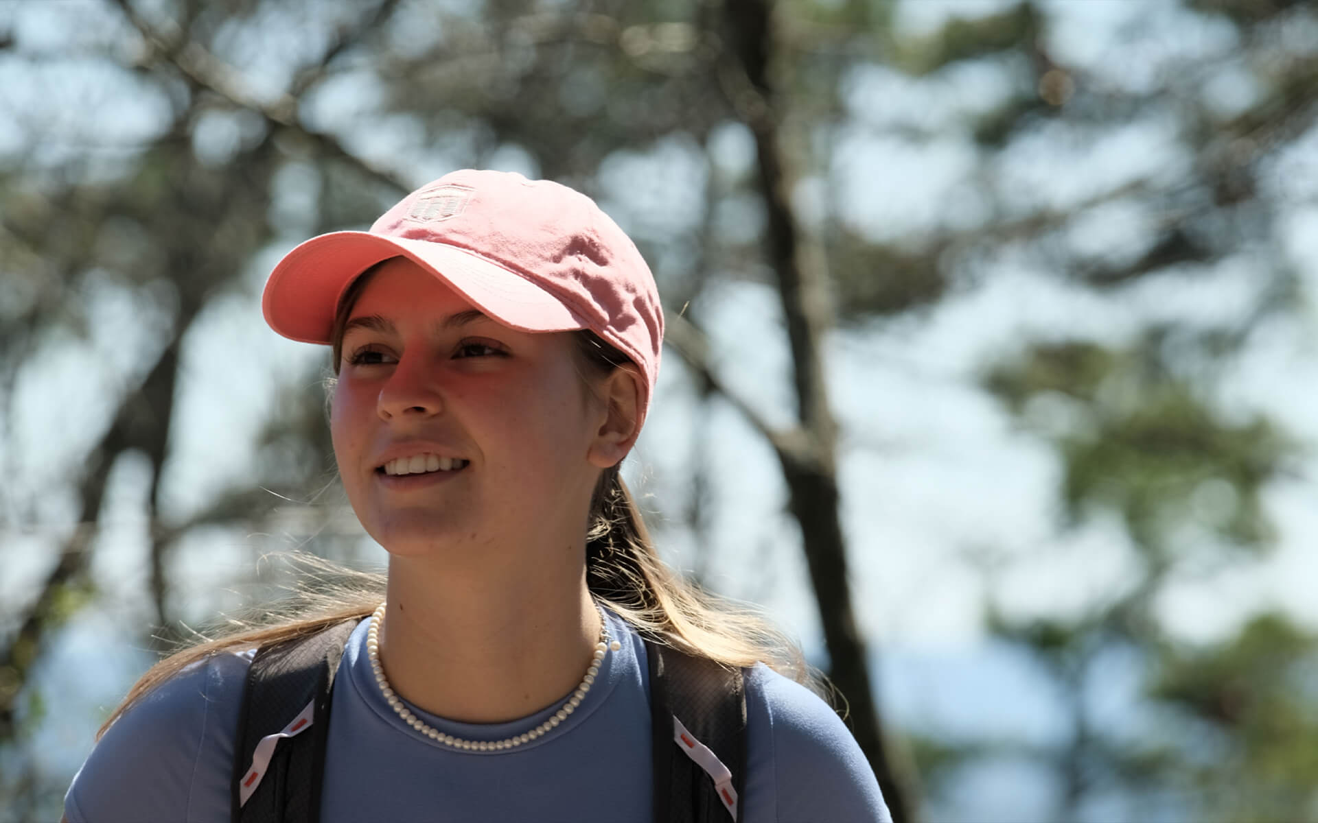 Woman walking in the woods wearing a pink armor bank hat.